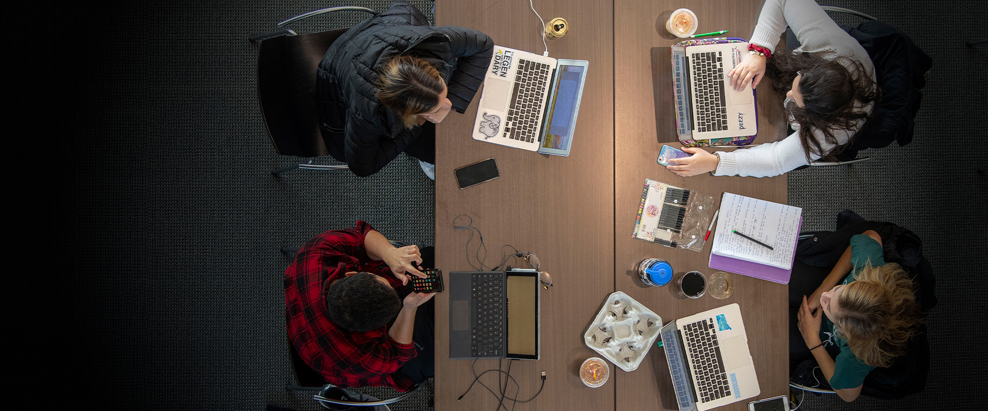 An overhead shot of four students at a table with computers and study materials.